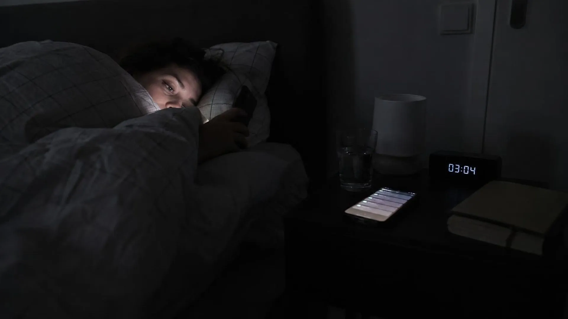 Een telefoon licht om drie uur 's nachts op met meldingen op een nachtkastje, de rest van de slaapkamer ligt in het donker.