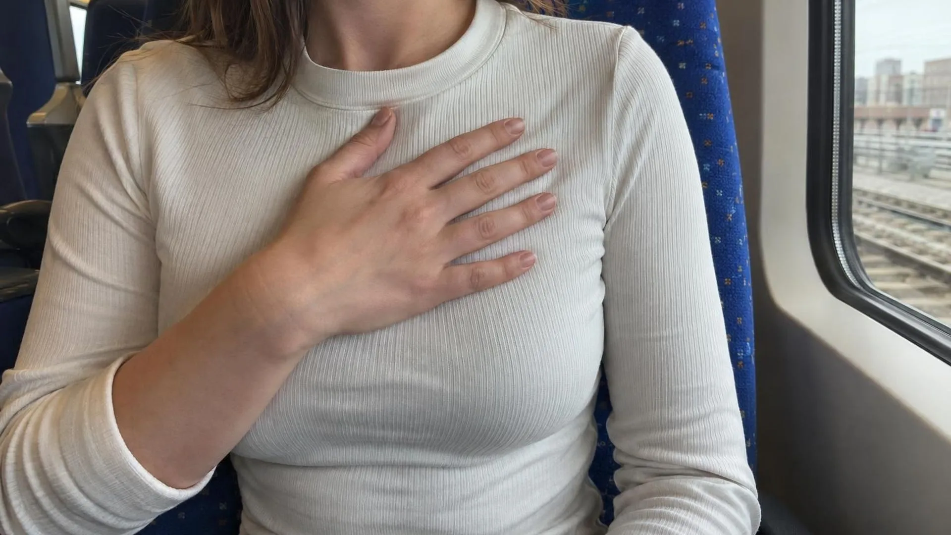 Close-up van een hand die tegen de borst drukt, zittend in een treinstoel