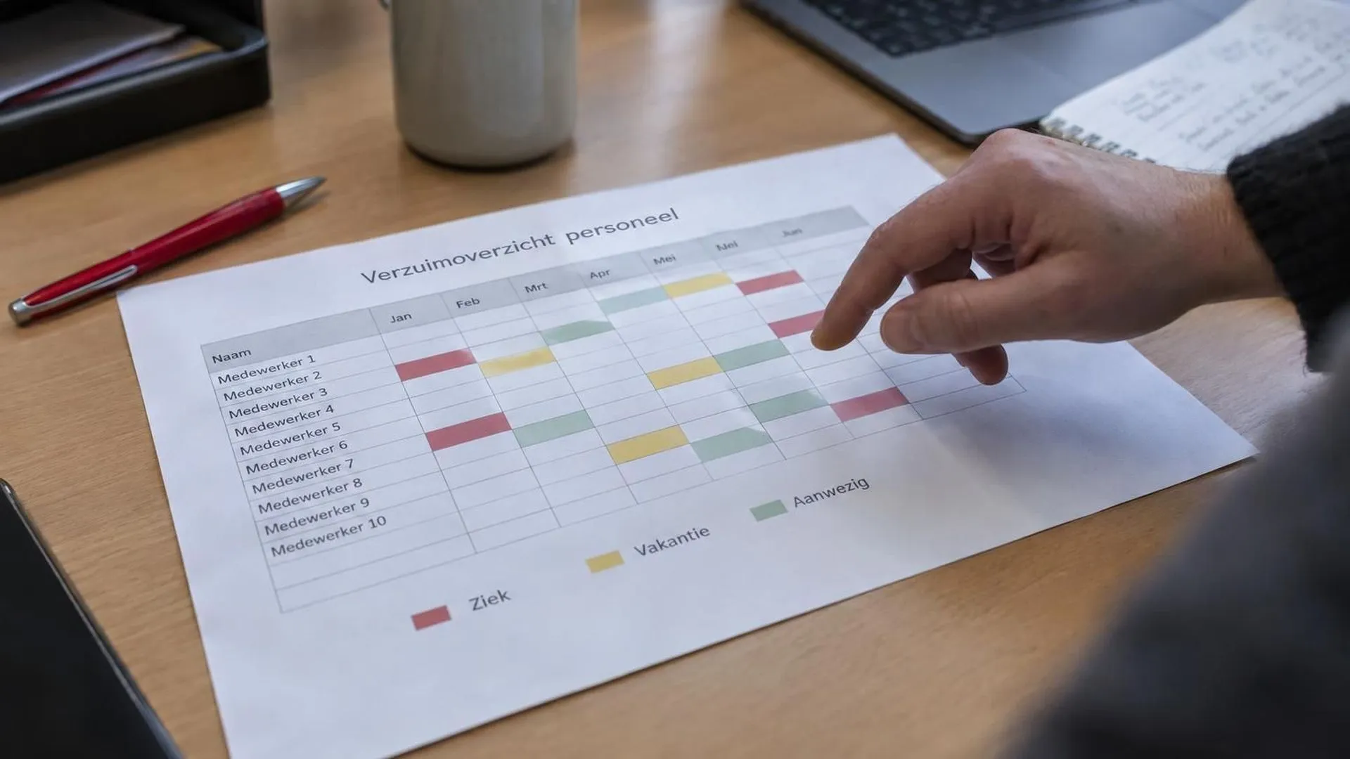 Een hand houdt een pen boven een uitgeprint verzuimoverzicht op een bureau op kantoor.