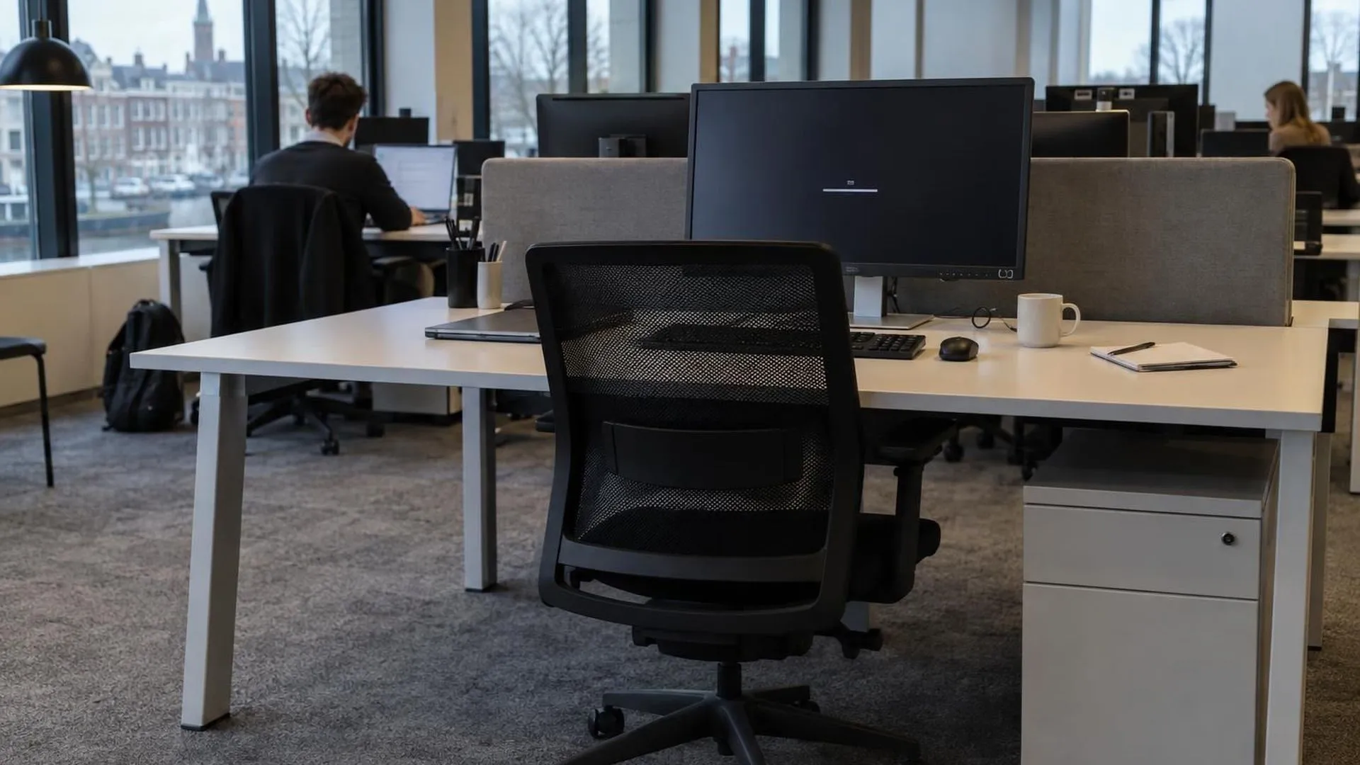 Een leeg bureau met stoel aangeschoven en een volle kop koffie op een maandagochtend, terwijl de rest van het kantoor gewoon doorwerkt.